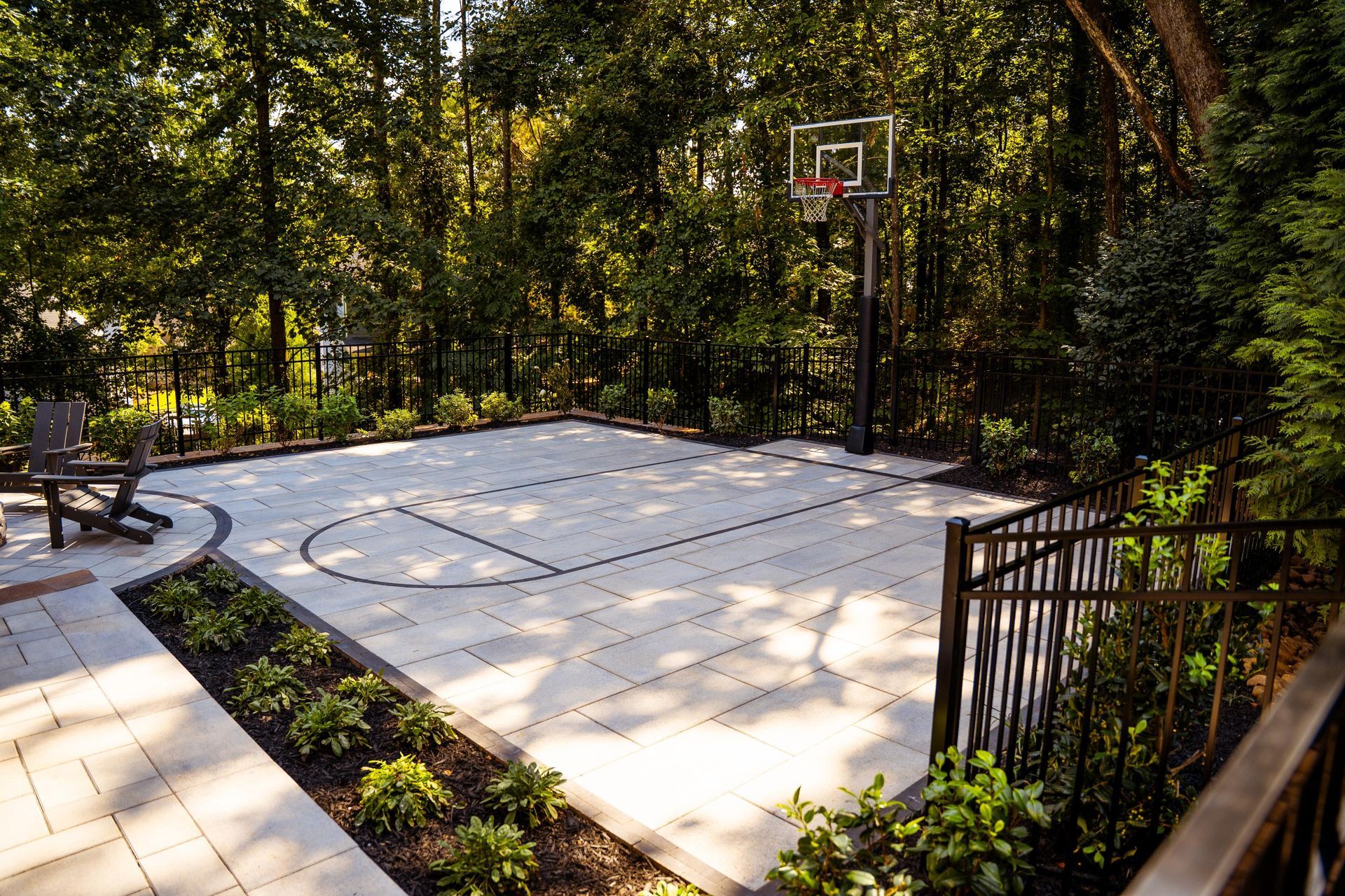 Outdoor basketball court with a paved surface and hoop, surrounded by trees and landscaping.