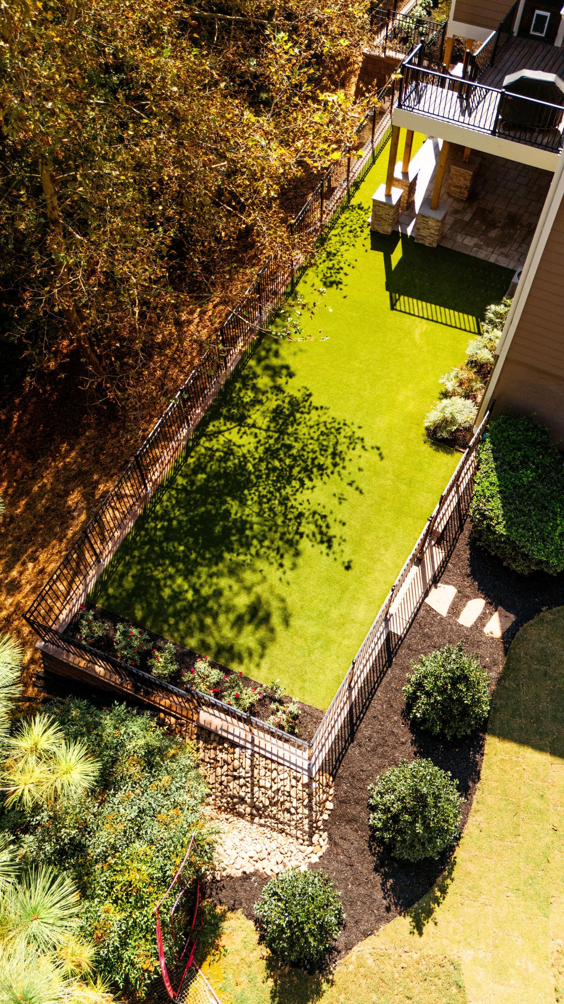 Aerial view of a rectangular green lawn surrounded by landscaping and a stone patio.