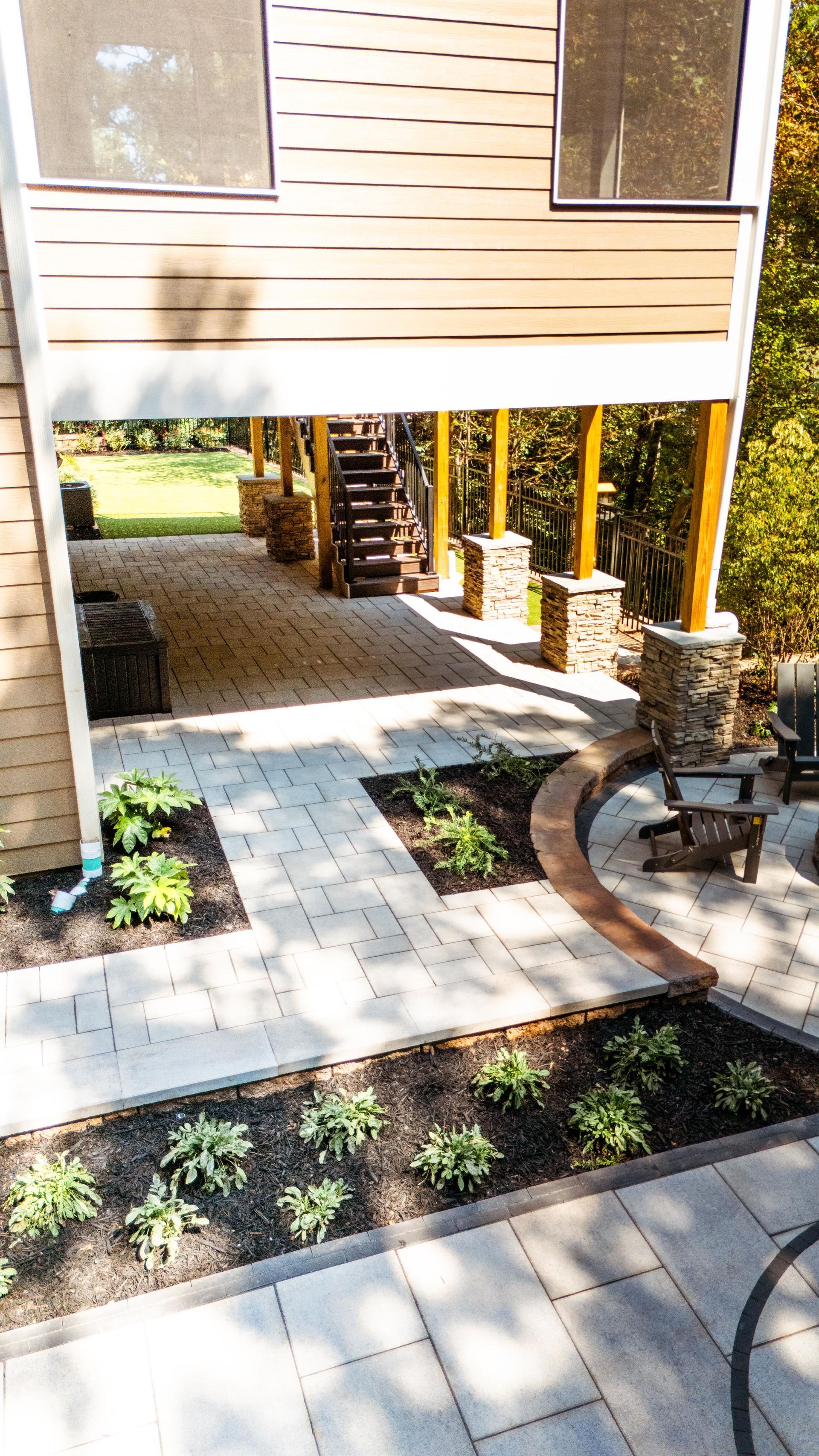 Stone patio and garden under a wooden deck, with stairs leading up.
