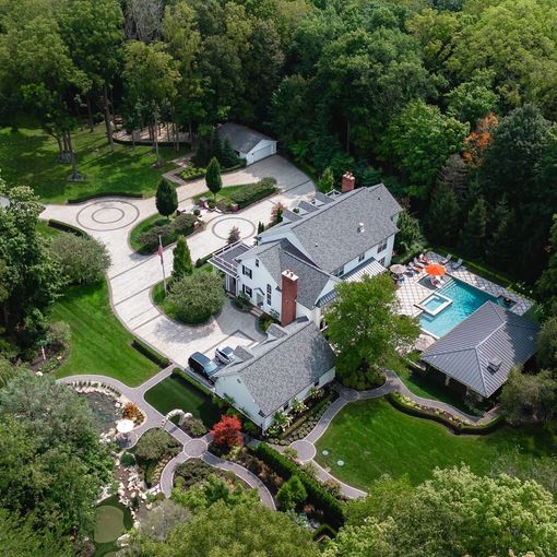 Aerial view of a large white house with a pool, surrounded by lush green trees and landscaping.