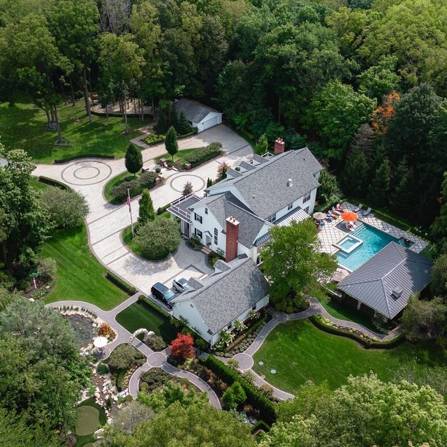 Aerial view of a large white house with a pool, surrounded by lush green trees and landscaping.
