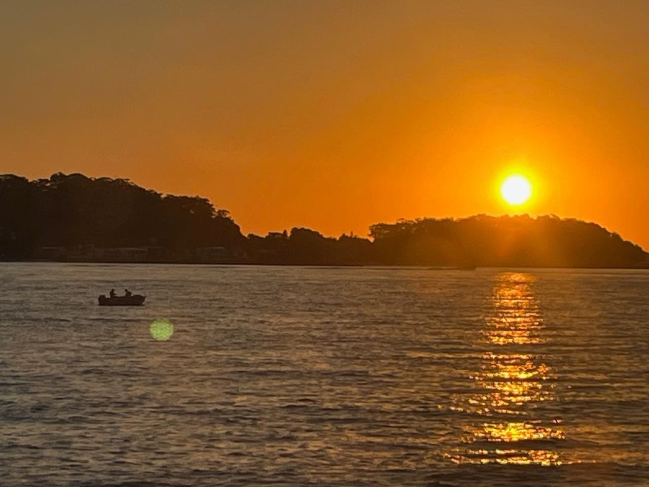 Sunset over water, small boat with people silhouetted, orange sky and sunlight reflecting on the water — YKnot Cruises in Nelson Bay, NSW