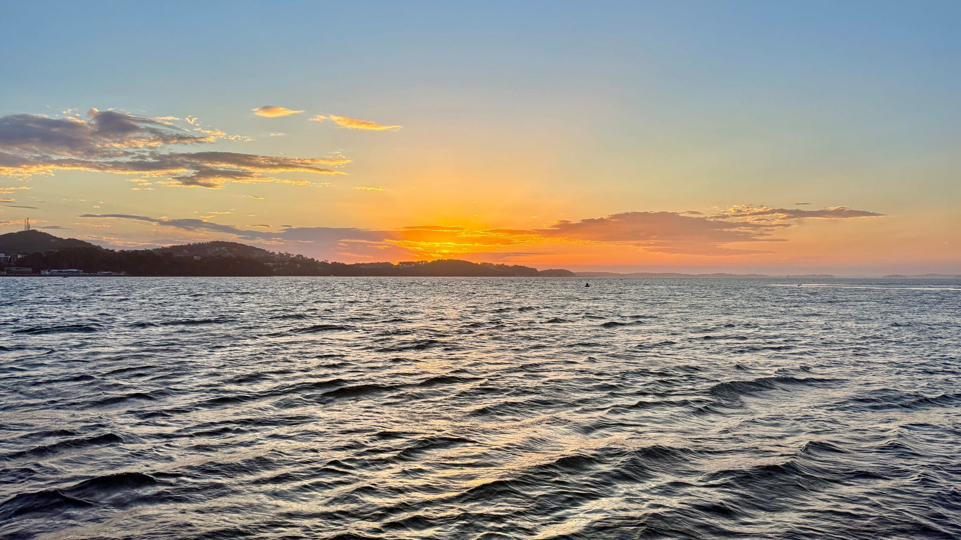 Sunset over ocean with golden light, clouds, and a distant shoreline.