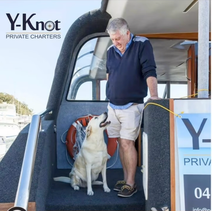 Man standing with a dog on a private charter boat steps, with Y-Knot Private Charters signage nearby
