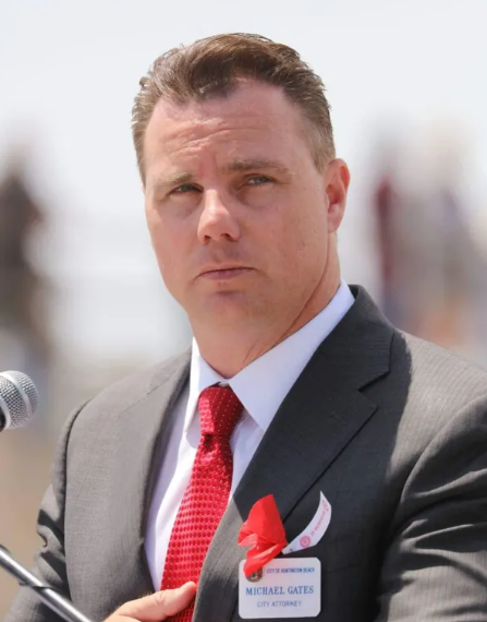 A man in a suit and tie stands in front of a microphone. Michael Gates, City Attorney