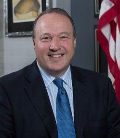A man in a suit and tie is smiling in front of an American flag. Scott Baugh