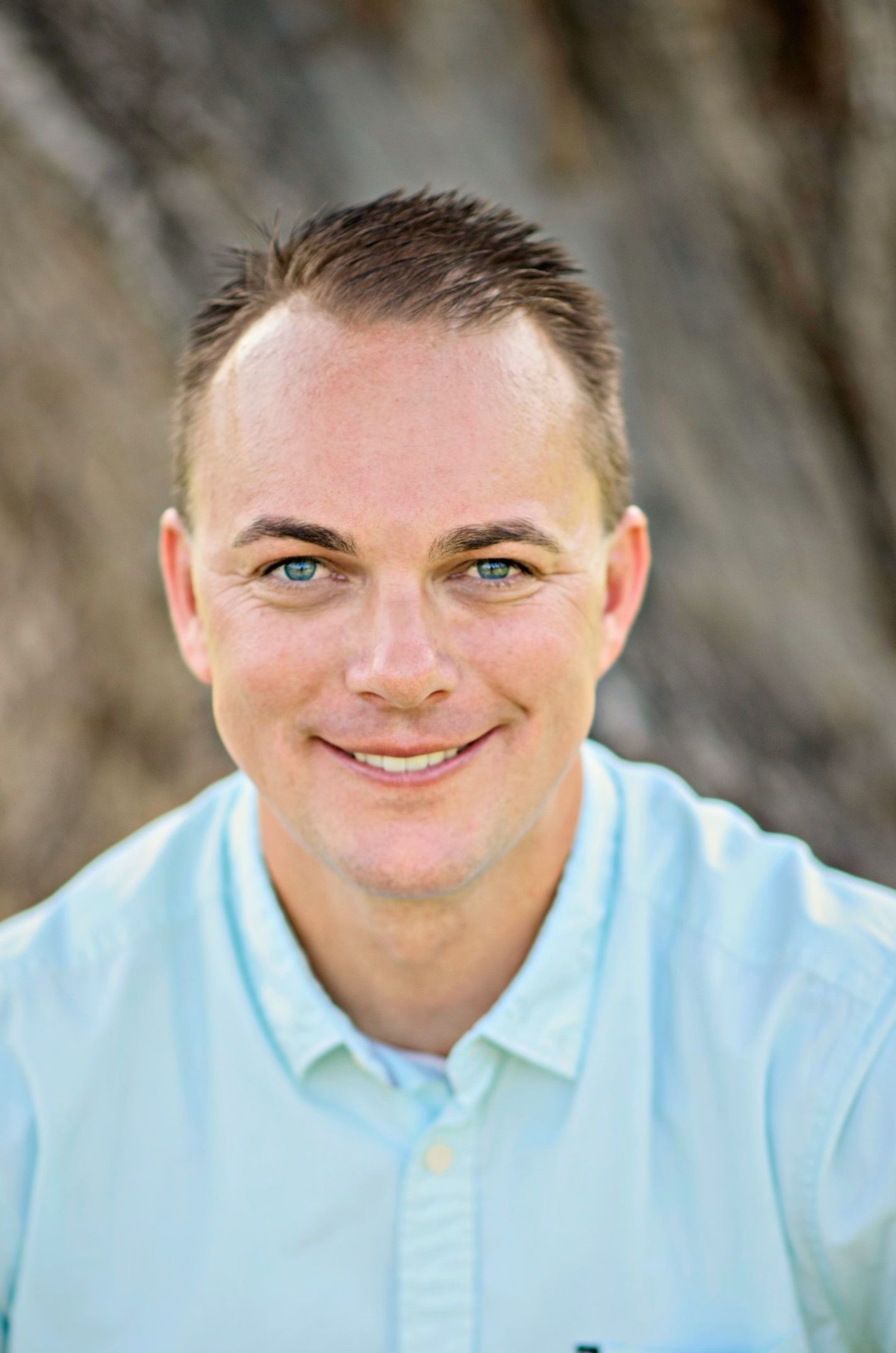 A man in a light blue shirt is smiling for the camera. Tim Shaw