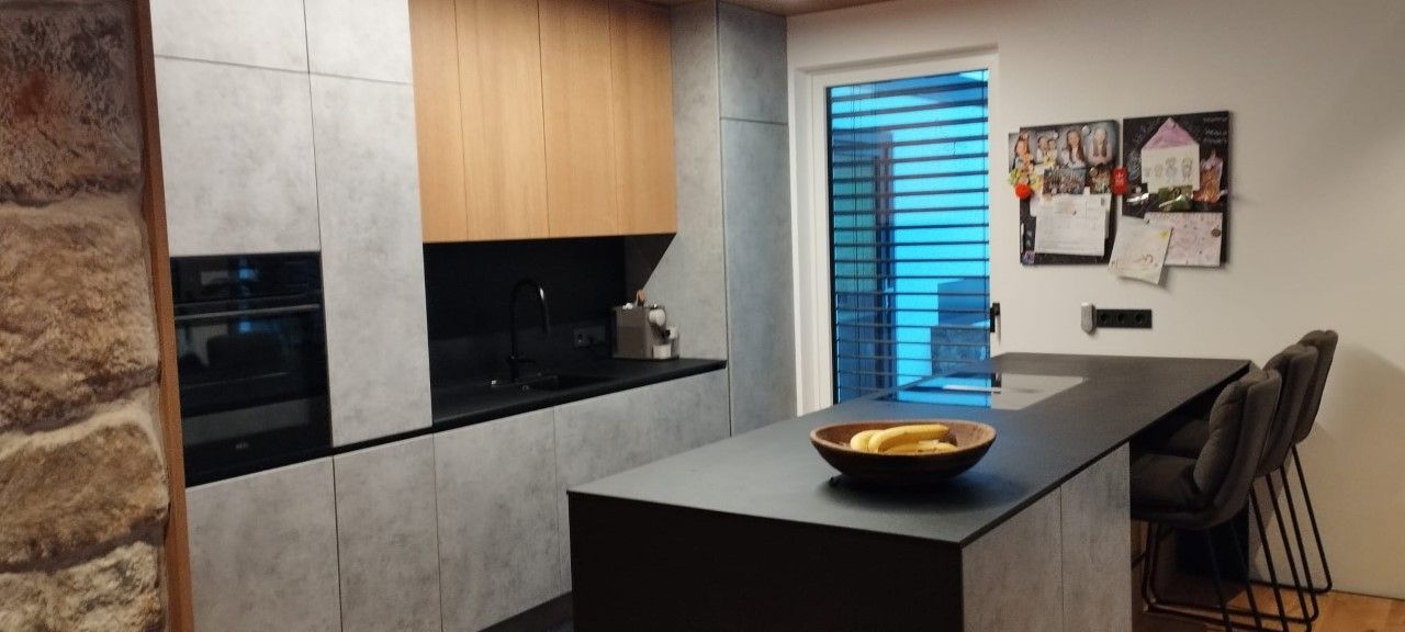 Moderne Küche mit hellgrauen Schränken, hölzernen Oberschränken, einer schwarzen Kochinsel mit Barhockern