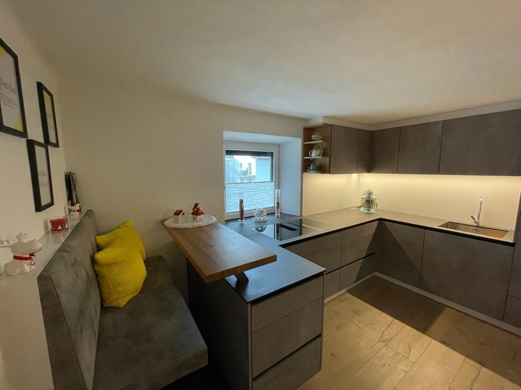 Moderne Küche mit dunklen Schränken, einer eingebauten Sitzbank mit gelben Kissen und einem Essbereich