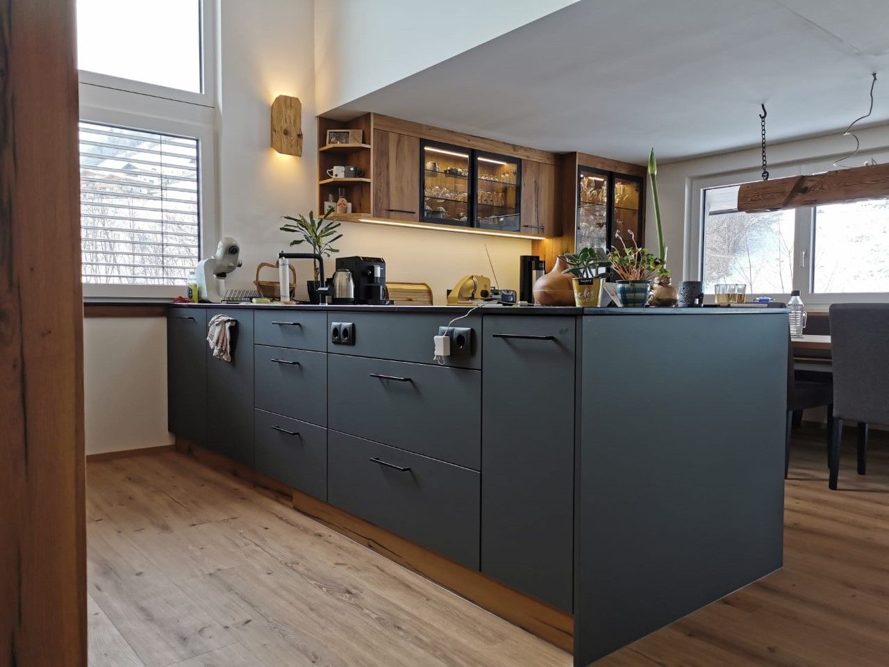 Moderne Kücheninsel mit mattschwarzen Schränken, Holzelementen und hellem Bodenbelag in einem geräumigen Raum.