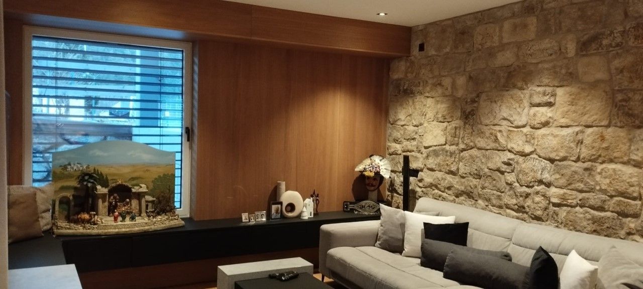 Ein Zimmer mit einem großen hellgrauen Sofa vor einer strukturierten Steinwand