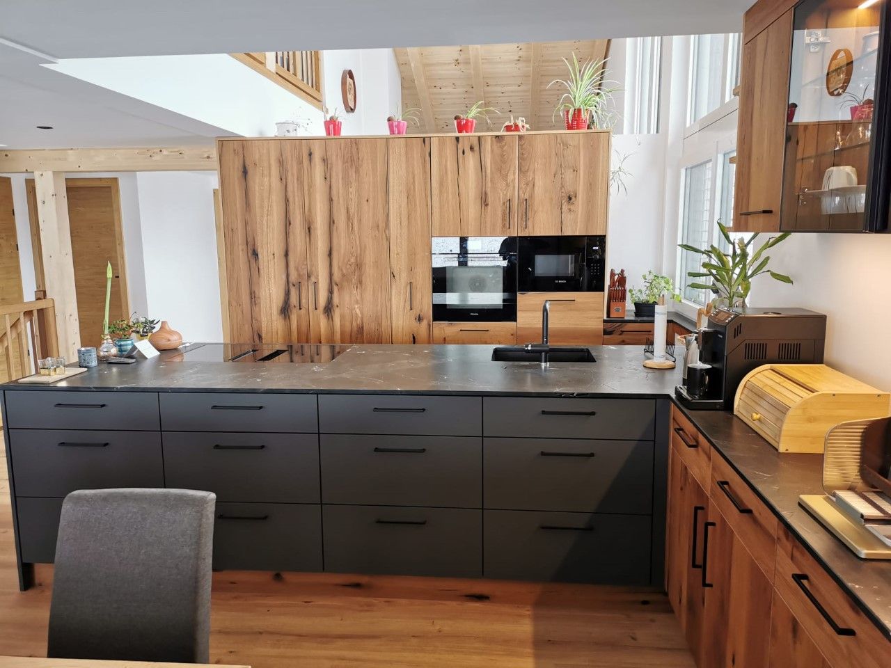 Moderne Küche mit schwarzer Kochinsel, dunkelgrauen Schubladen, Holzschränken und Spüle in einem offenen Wohnbereich.