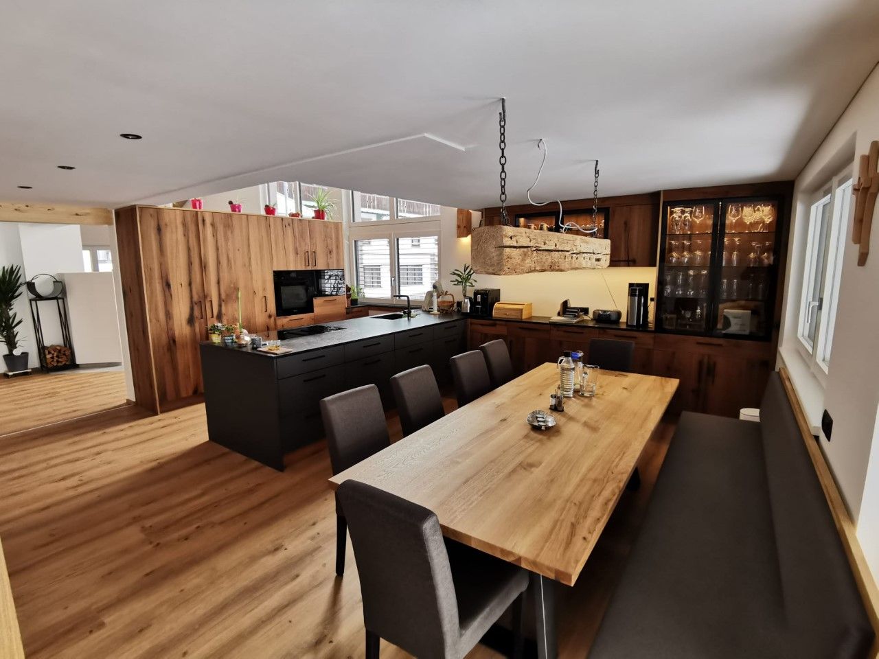 Moderne Küche und Essbereich mit langem Holztisch, dunklen Stühlen, einer Bank und Naturholzschränken.