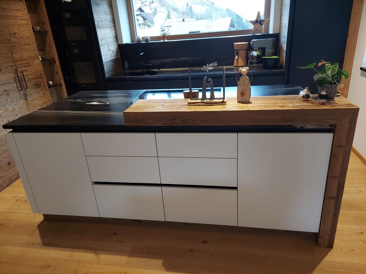 Eine moderne Kücheninsel mit weißen Schränken, einer schwarzen Arbeitsplatte und einer Frühstücksbar