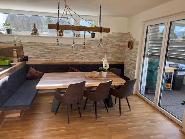 Eine moderne Essecke mit Holztisch, dunkel gepolsterter Bank, drei Stühlen und einer rustikalen Balken-Pendelleuchte.