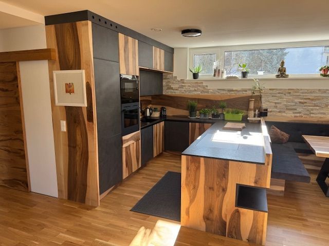 Moderne Küche mit Naturholzschränken und dunklen, matten Oberflächen, mit Kochinsel und eingebauten Geräten.