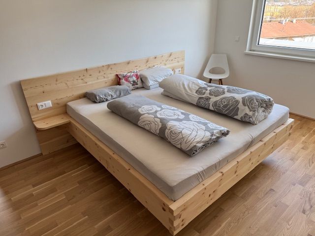 Ein minimalistisches Bettgestell aus hellem Holz mit zwei gemusterten grauen Bettdecken