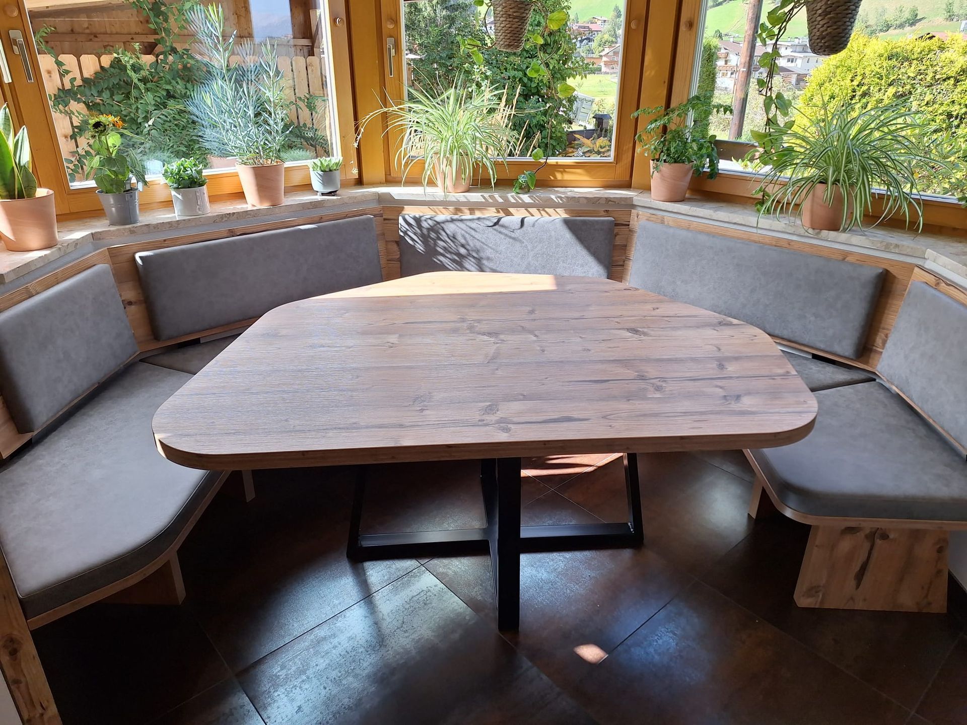 In einem sonnendurchfluteten Raum mit Pflanzen steht ein Esstisch aus Holz