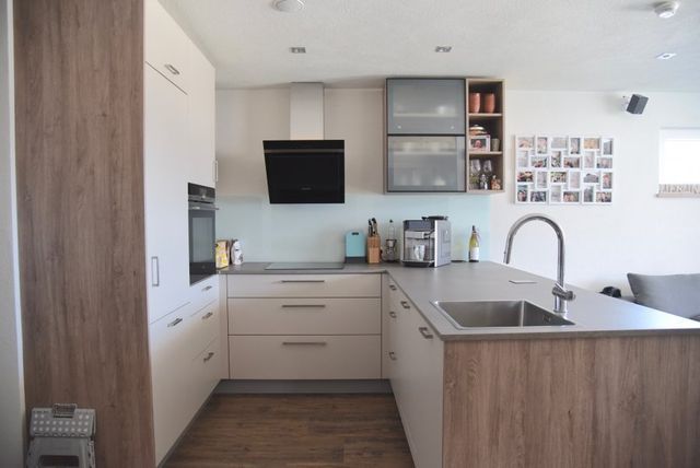 Eine moderne Küche mit hellen Schränken, Akzenten in Holzoptik, einer Kochinsel mit Spüle und Edelstahlgeräten.