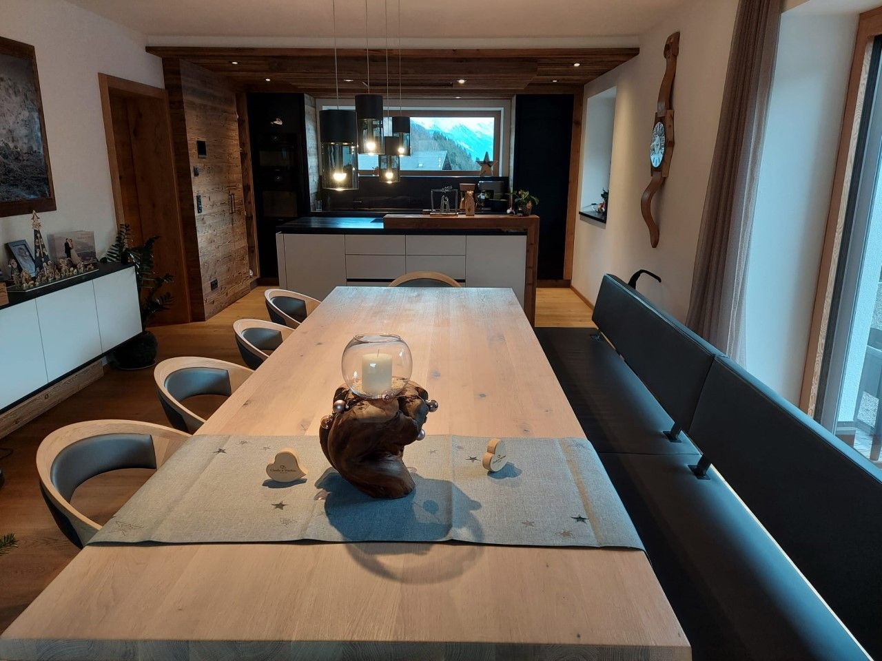 Ein modernes Esszimmer mit einem langen Holztisch, einer Sitzbank, mehreren Stühlen und einer offenen Küche