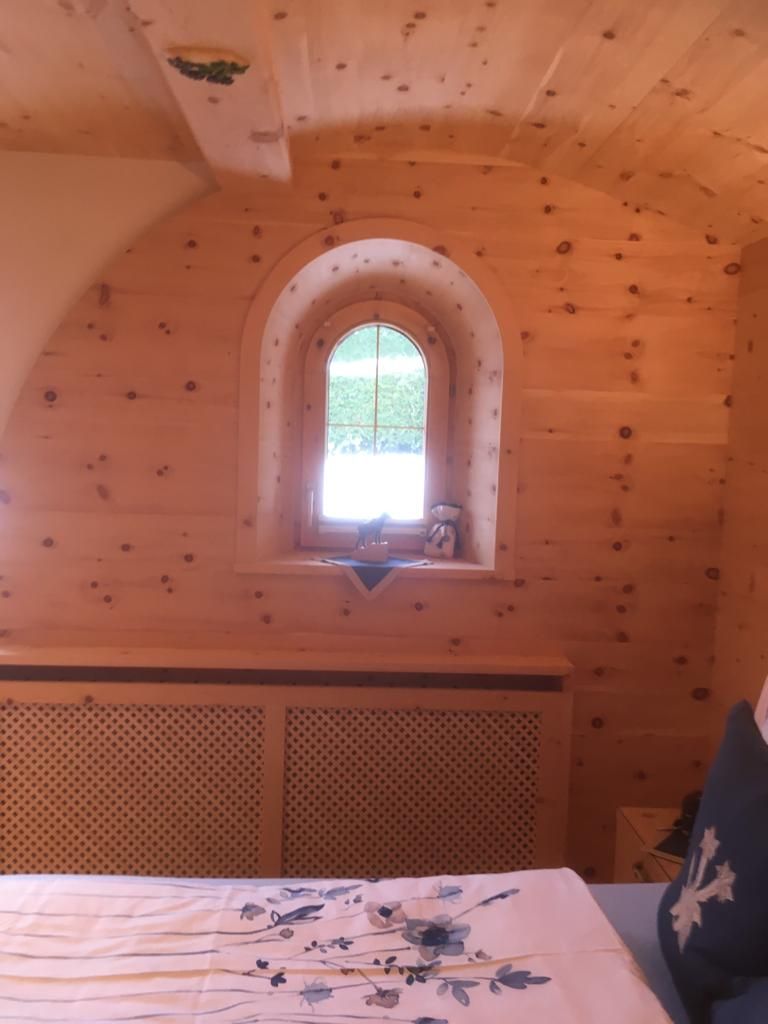 Ein kleines, bogenförmiges Fenster in einer mit Kiefernholz getäfelten Wand