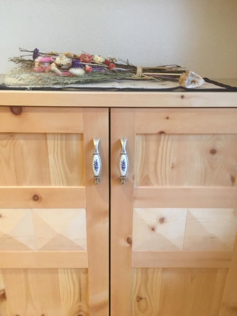 Ein heller Holzschrank mit blumengemusterten Keramikgriffen