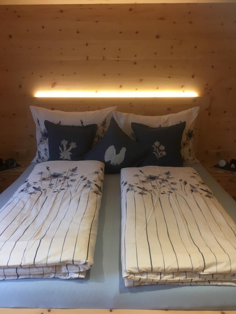 Ein gemütliches Schlafzimmer mit Holzwänden, einem Doppelbett mit geblümter Bettwäsche und dunkelblauen Zierkissen.