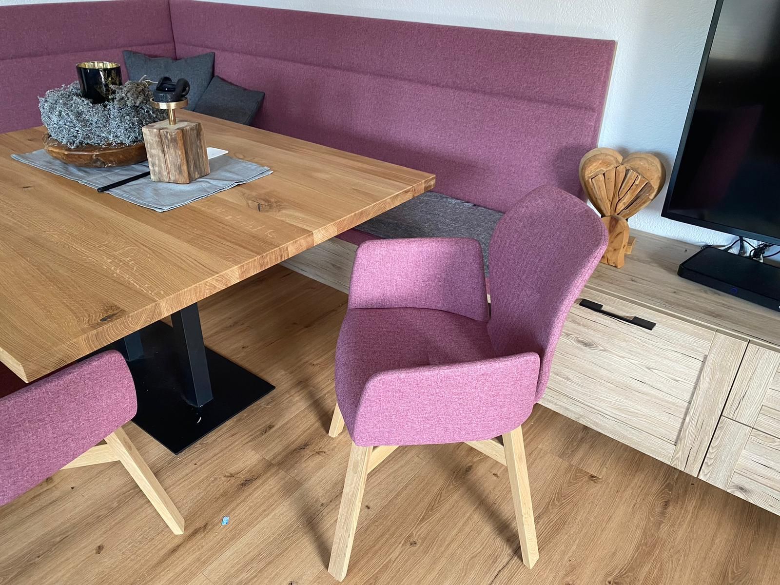 Ein Esstisch aus Holz mit lila gepolsterten Stühlen und einer Eckbank in einem hell erleuchteten Raum.