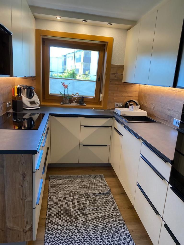 Eine U-förmige Küche mit weißen Schränken, dunklen Arbeitsplatten