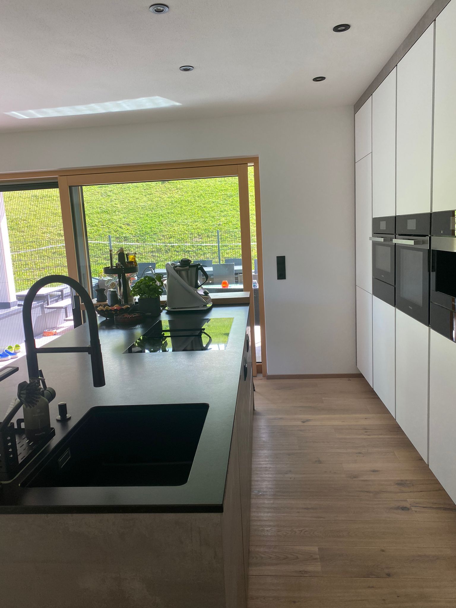 Eine moderne Küche mit einer dunklen Kochinsel mit Spüle und Herd, weißen Hochschränken