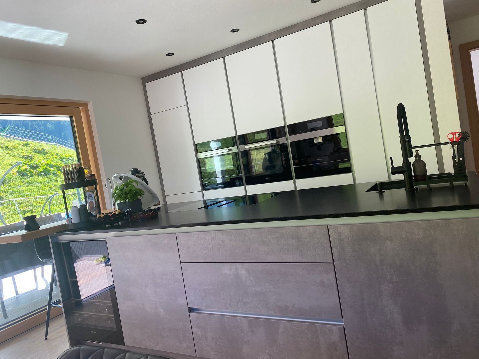 Moderne Küche mit einer großen grauen Kochinsel, weißen Schränken, Einbaubacköfen