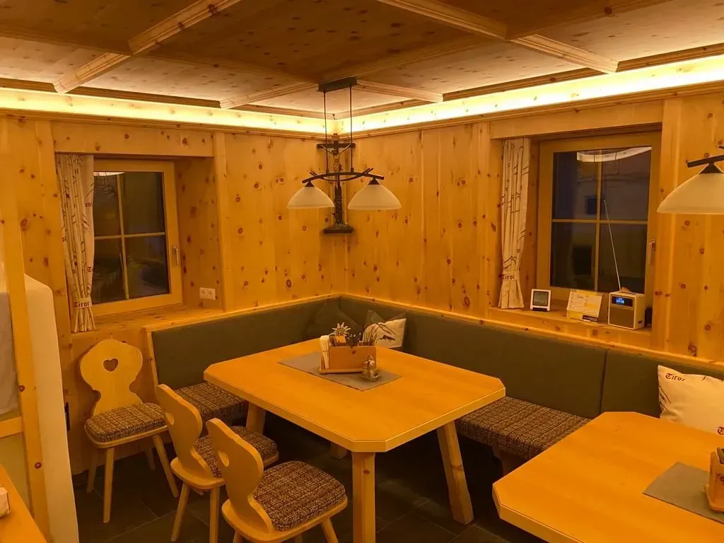 Eine gemütliche Essecke mit Holzwänden, einem hellen Holztisch, einer grünen Eckbank und dazu passenden gemusterten Stühlen.