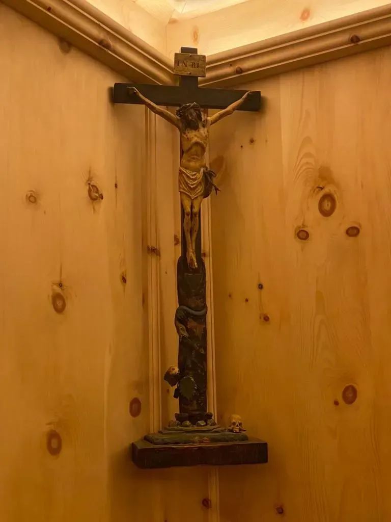 Ein in einer Holzecke angebrachtes Kruzifix mit einer detaillierten Darstellung Jesu an einem dunklen, rustikalen Kreuz.