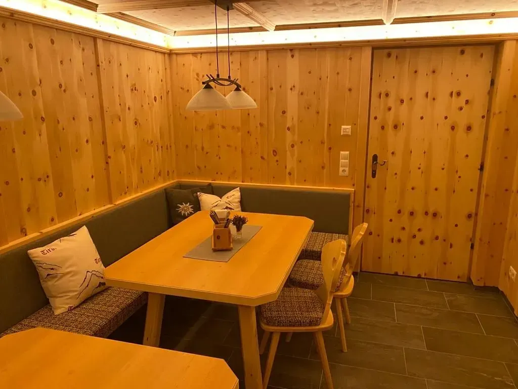 Eine gemütliche Essecke aus Holz mit Eckbank, Tisch und zwei Stühlen, vor hellen Holzwänden und Steinboden.