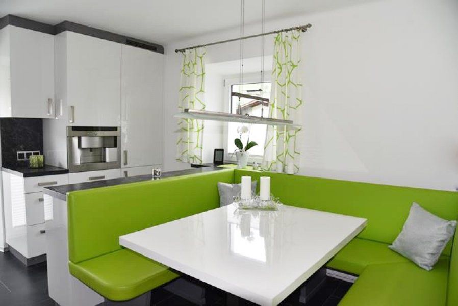 Eine moderne weiße Küche besticht durch eine leuchtend grüne, L-förmige Eckbank und einen weißen Tisch mit zwei Kerzen.