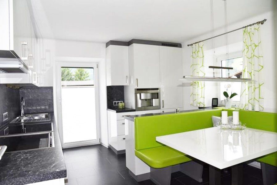 Moderne Küche mit weißen Schränken, dunklen Arbeitsplatten und einer limettengrünen Eckbank mit weißem Tisch.