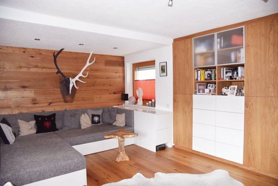 Ein gemütliches Wohnzimmer mit grauer Eckcouch, holzgetäfelter Wand