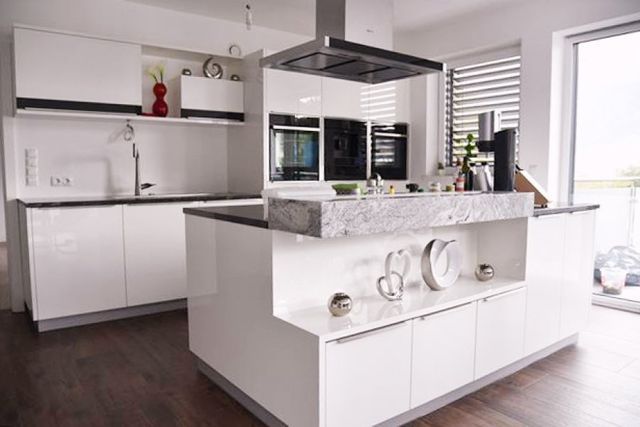 Moderne weiße Küche mit Kochinsel, Arbeitsplatten aus Stein, integrierten Geräten und minimalistischer Einrichtung.