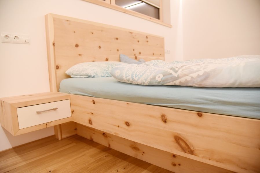 Ein hölzernes Bettgestell mit passendem schwebendem Nachttisch, hellblauer Bettwäsche und weißer Schubladenfront.