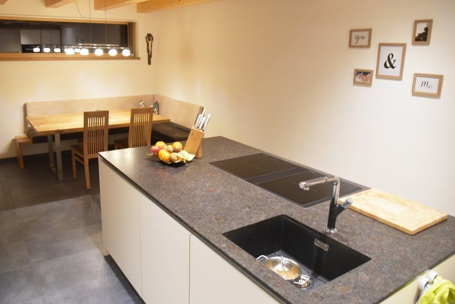 Eine moderne Küche mit einer großen Kochinsel mit Spüle und Kochfeld, die sich vor einer hölzernen Essecke befindet.