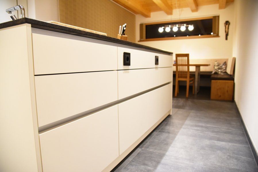 Eine moderne, cremefarbene Kücheninsel mit dunkler Arbeitsplatte, gegenüber einem Essbereich mit Holzmöbeln.