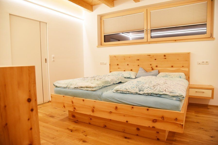 Ein modernes Schlafzimmer mit einem Bettgestell aus Kiefernholz, hellblauer Bettwäsche, Holzboden und einem großen Fenster.