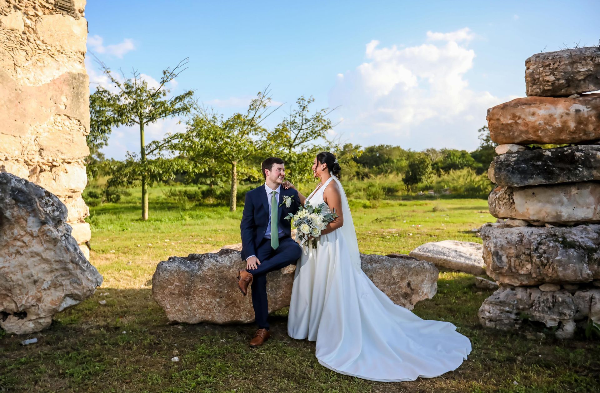 A bride and groom are sitting on rocks in a field.