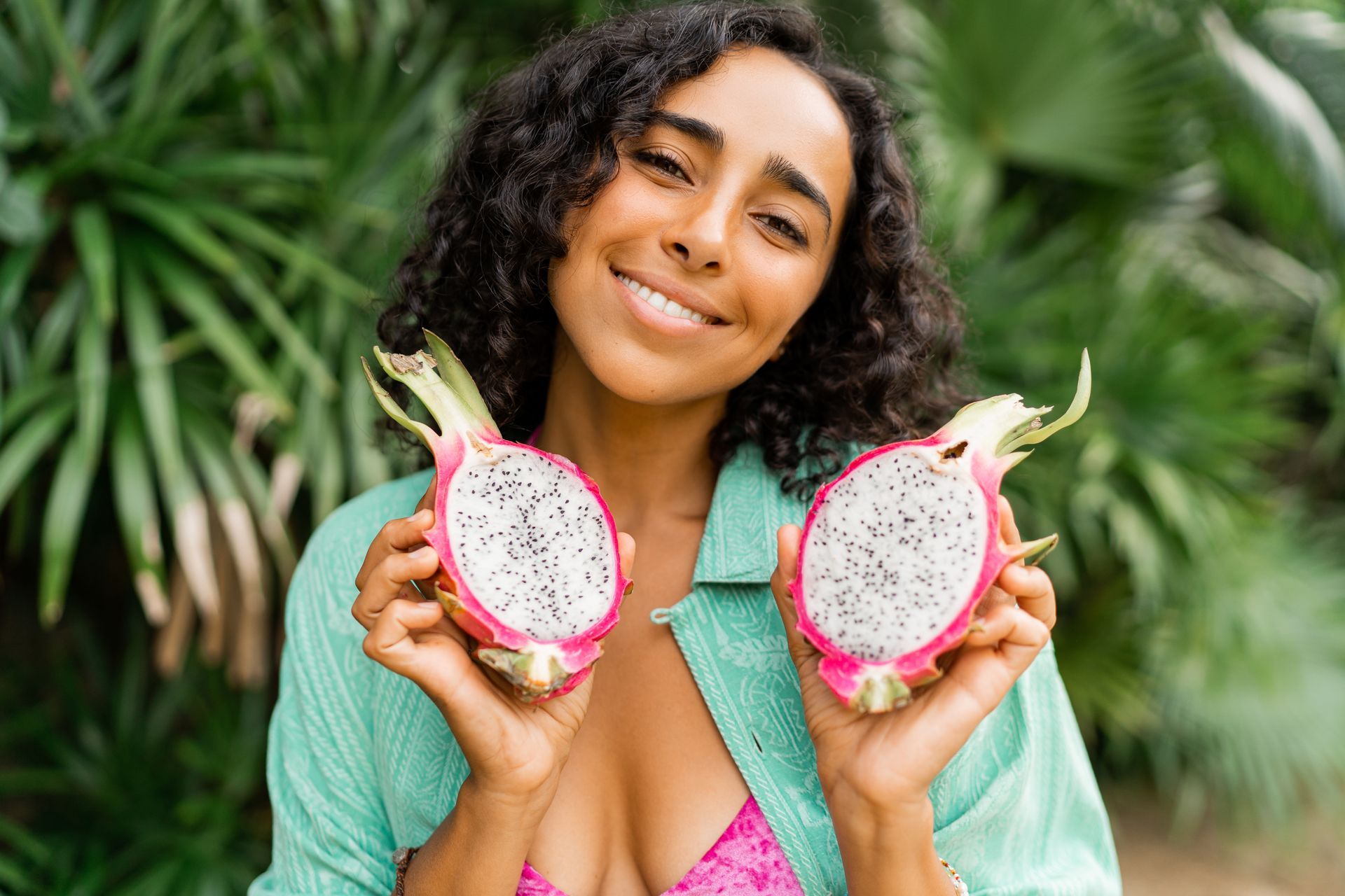 A woman is holding two dragon fruits in her hands and smiling.