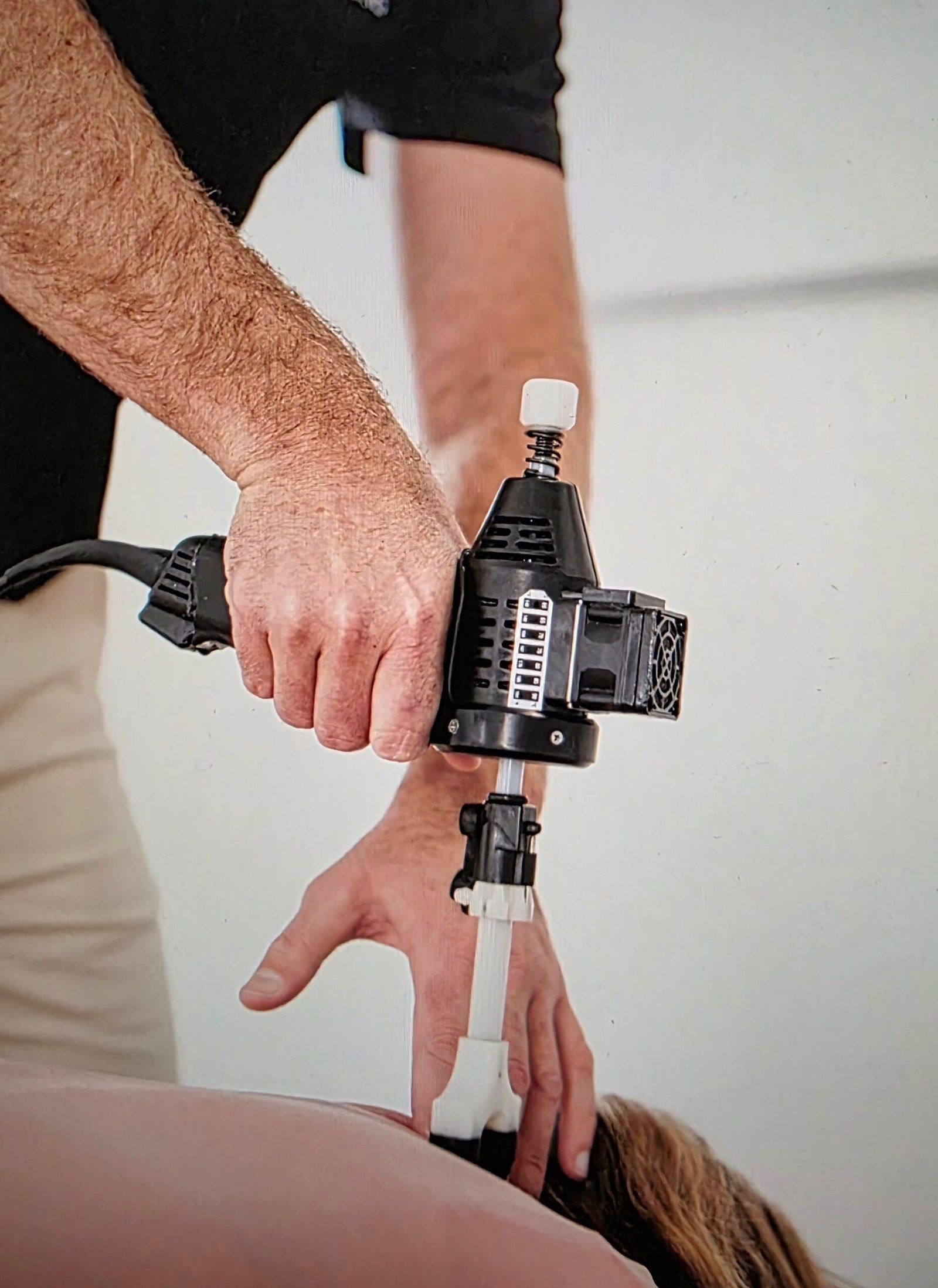 Person using a chiropractic adjusting tool on another person's back.