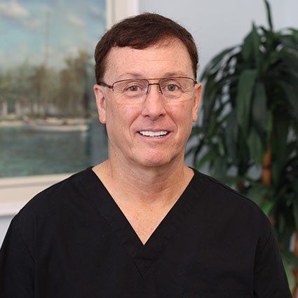 Man in glasses, black scrubs, smiling in a dental office.