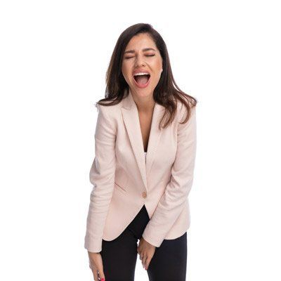 Woman laughing, eyes closed, mouth open, wearing a pink blazer and black pants.