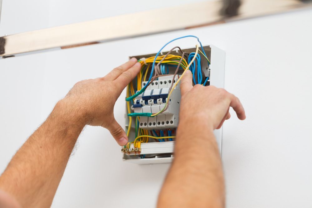 A Man Is Working On An Electrical Box On A Wall — In Electrics In Tully, QLD