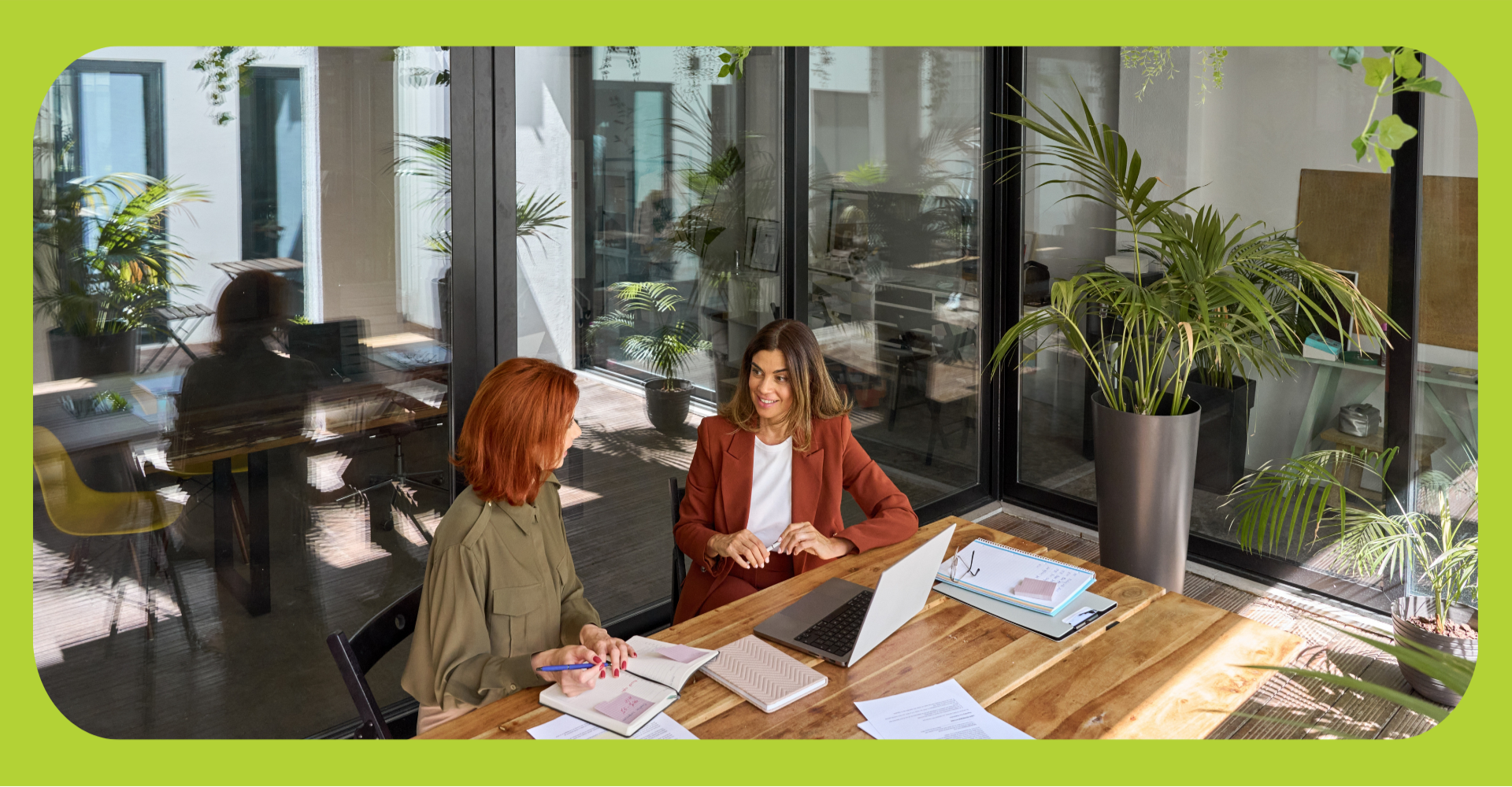 Two women are sitting at a table with a laptop, discussing the benefits and drawbacks of transferring property into an llc