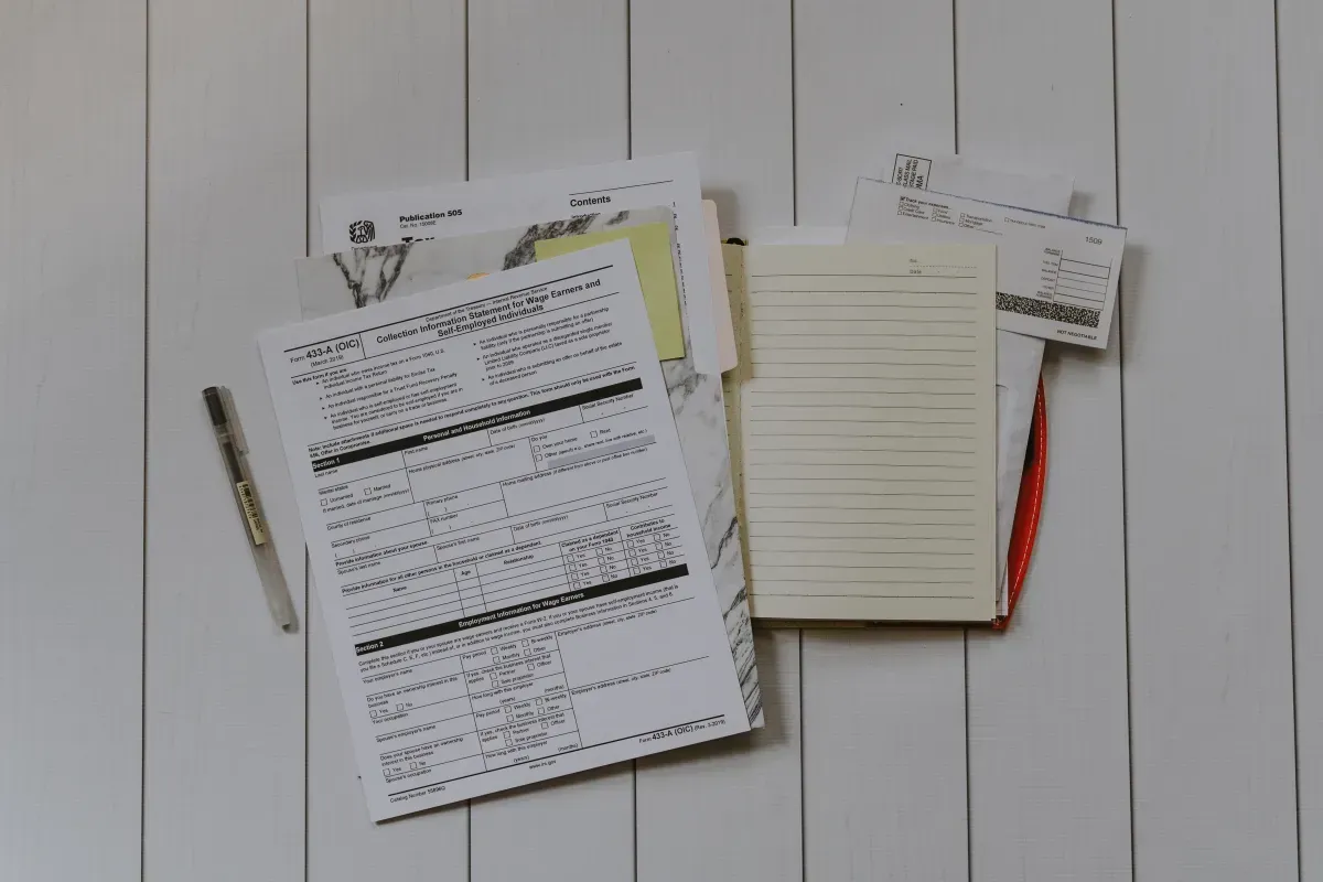 A stack of papers and notebooks on a wooden table.